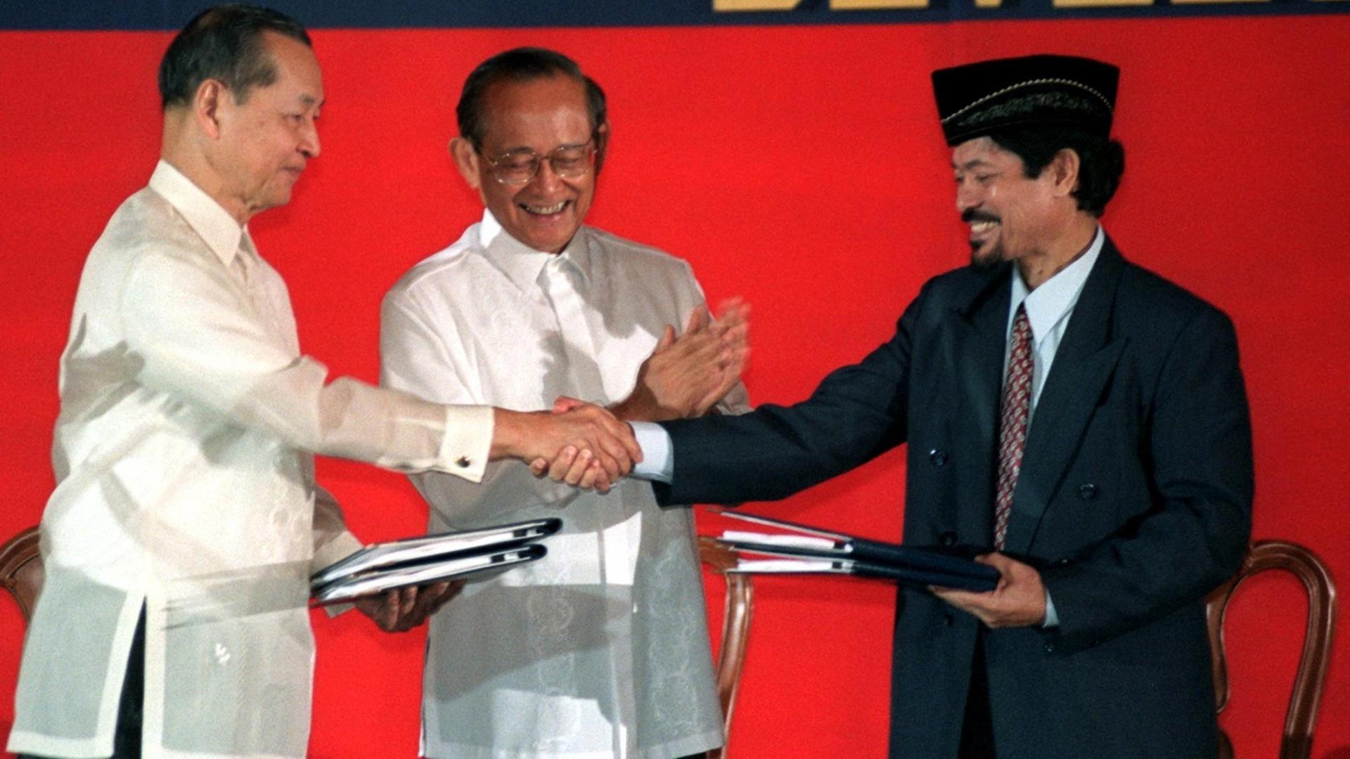 Der philippinische Präsident Fidel Ramos (M) applaudiert, als der Chefunterhändler der Regierung, Manuel Yan (l), und der Vorsitzende der Nationalen Moro-Befreiungsfront (MNLF), Nur Misuari (r), am 2.9.1996 im Malacanang-Palast in Manila nach Unterzeichnung des Friedensvertrages die Urkunden austauschen. Der philippinische Präsident Fidel Ramos (M) applaudiert, als der Chefunterhändler der Regierung, Manuel Yan (l), und der Vorsitzende der Nationalen Moro-Befreiungsfront (MNLF), Nur Misuari (r), am 2.9.1996 im Malacanang-Palast in Manila nach Unterzeichnung des Friedensvertrages die Urkunden austauschen.