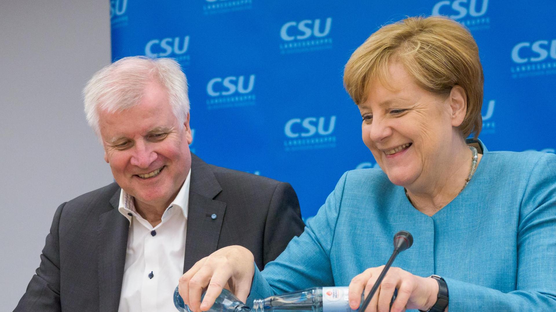 Bundeskanzlerin Merkel und CSU-Chef Seehofer sitzen nebeneinander, Merkel gießt Wasser aus zwei Flaschen in ein Glas. Bundeskanzlerin Merkel und CSU-Chef Seehofer sitzen nebeneinander, Merkel gießt Wasser aus zwei Flaschen in ein Glas.