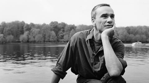 Eine schwarz-weiß Aufnahme des Schauspielers Ingo Hülsmann, am Ufer sitzend.