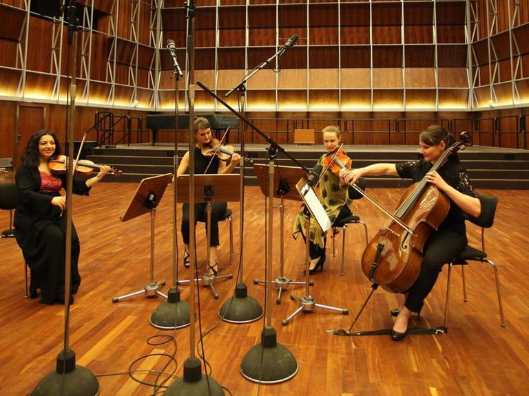 Das Quartett aus vier jungen Musikerinnen sitzt in einem leer geräumten Konzertsaal.