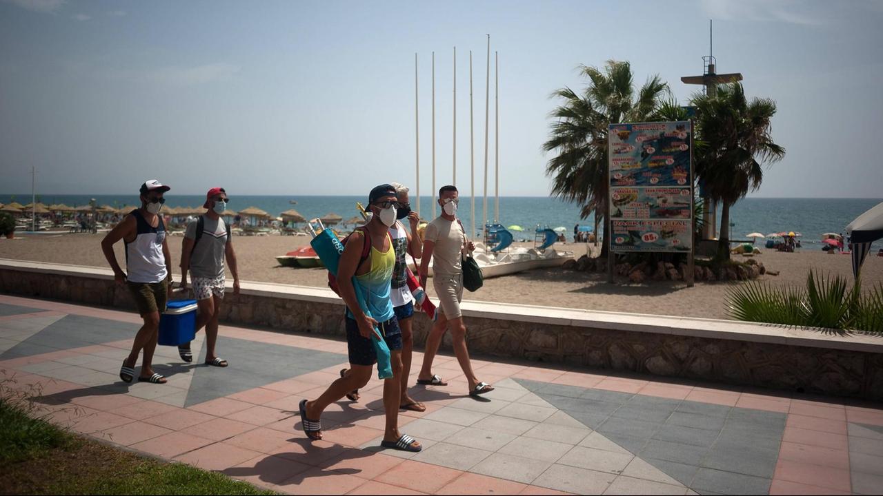 Urlaub in Corona-Zeiten am Strand von Torremolinos in Spanien. Mehrere Menschen laufen mit Mund-Nase-Maske an der Promenade entlang. Urlaub in Corona-Zeiten am Strand von Torremolinos in Spanien. Mehrere Menschen laufen mit Mund-Nase-Maske an der Promenade entlang.