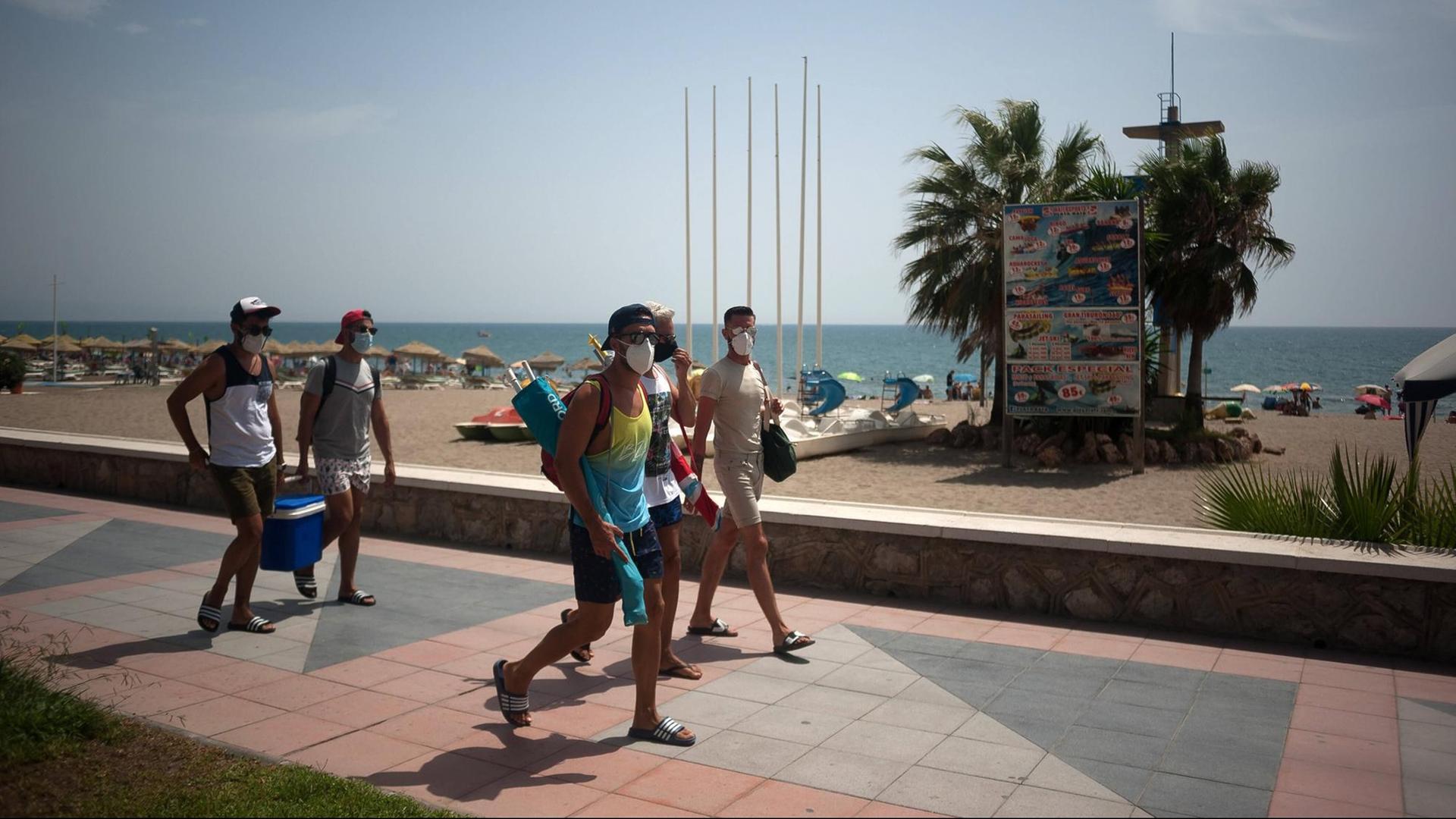 Urlaub in Corona-Zeiten am Strand von Torremolinos in Spanien. Mehrere Menschen laufen mit Mund-Nase-Maske an der Promenade entlang. Urlaub in Corona-Zeiten am Strand von Torremolinos in Spanien. Mehrere Menschen laufen mit Mund-Nase-Maske an der Promenade entlang.