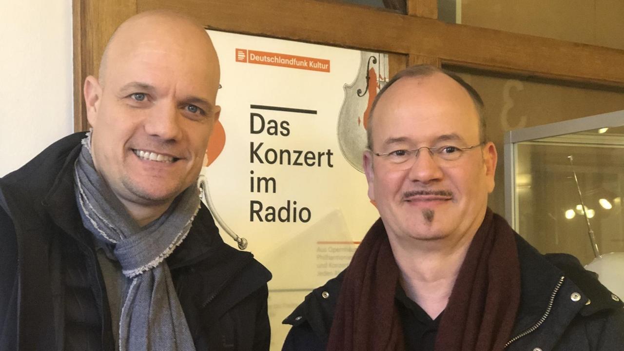 Die beiden Männer stehen im Foyer des Hauses vor einem Plakat des Senders. Die beiden Männer stehen im Foyer des Hauses vor einem Plakat des Senders.