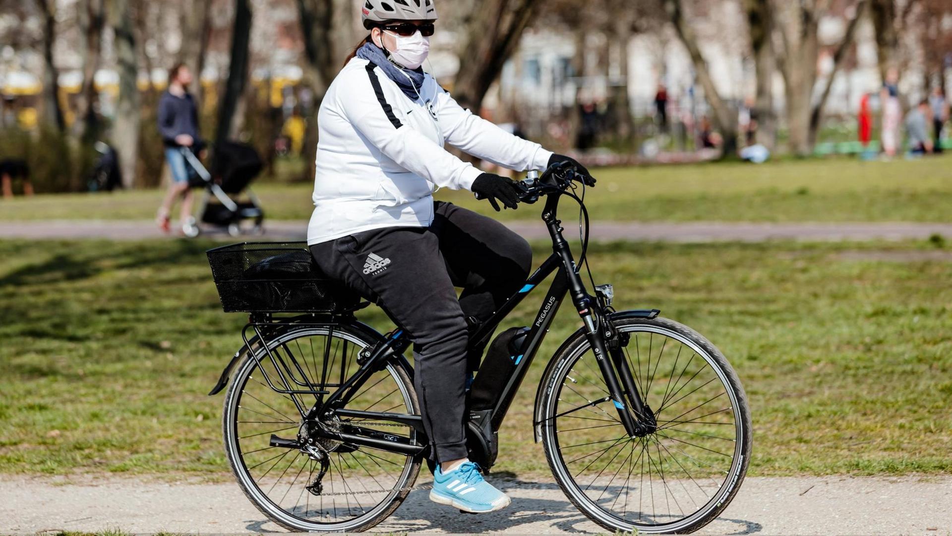 Eine Frau fährt auf ihrem Rad mit Mundschutz durch Berlin. Eine Frau fährt auf ihrem Rad mit Mundschutz durch Berlin.
