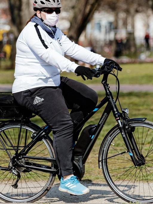Eine Frau fährt auf ihrem Rad mit Mundschutz durch Berlin.