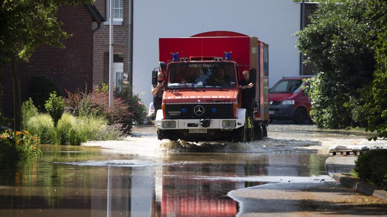 Ein Einsatzfahrzeug der Feuerwehr fährt über eine überflutete Straße in Steinkirchen, westlicher Ortsteil der Stadt Wassenberg (Kreis Heinsberg). Der Ort liegt in der Nähe der Rur.