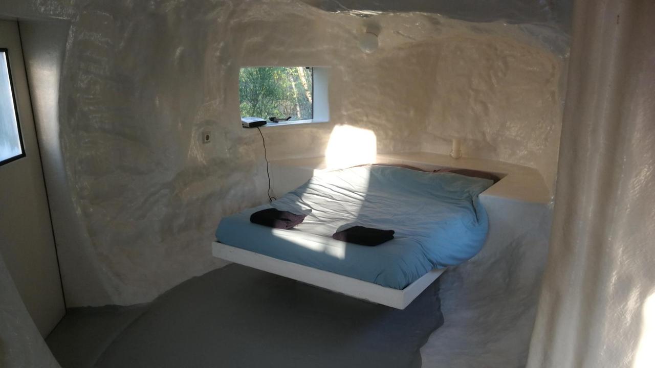 Spartanische Einrichtung mit Bett und weißen Wänden: Das Werk "CasAnus" von Joep van Lieshout auf dem Gelände der Verbeke Foundation Spartanische Einrichtung mit Bett und weißen Wänden: Das Werk "CasAnus" von Joep van Lieshout auf dem Gelände der Verbeke Foundation