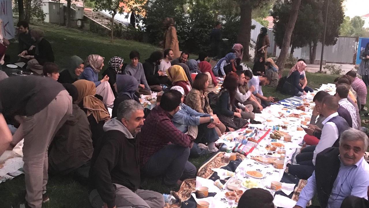 Viele Menschen sitzen zum Fasten-Brechen an einem langen Tisch mit Essen darauf. Viele Menschen sitzen zum Fasten-Brechen an einem langen Tisch mit Essen darauf.