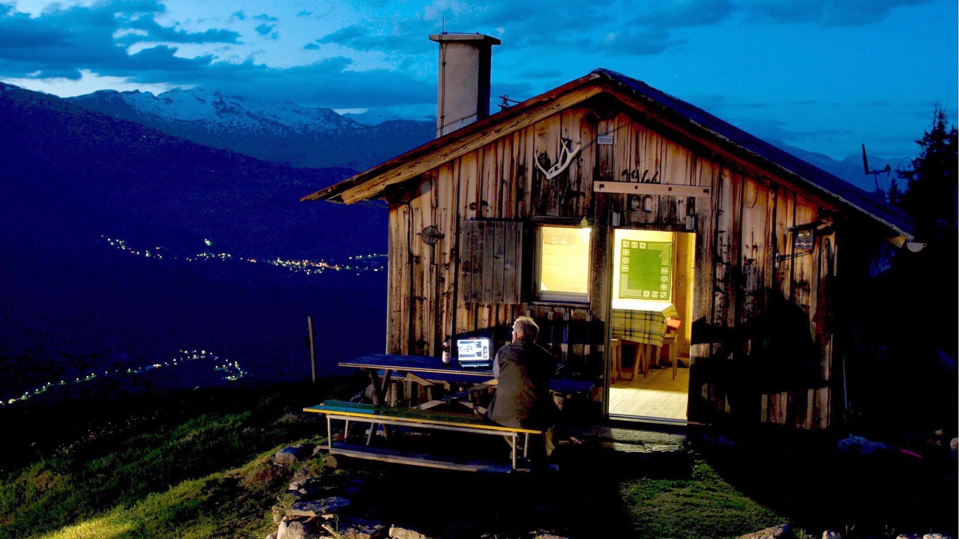 Ein Schäfer in Obersaxen in der Schweiz schaut Fernsehen in den Bergen vor seiner Almhütte.