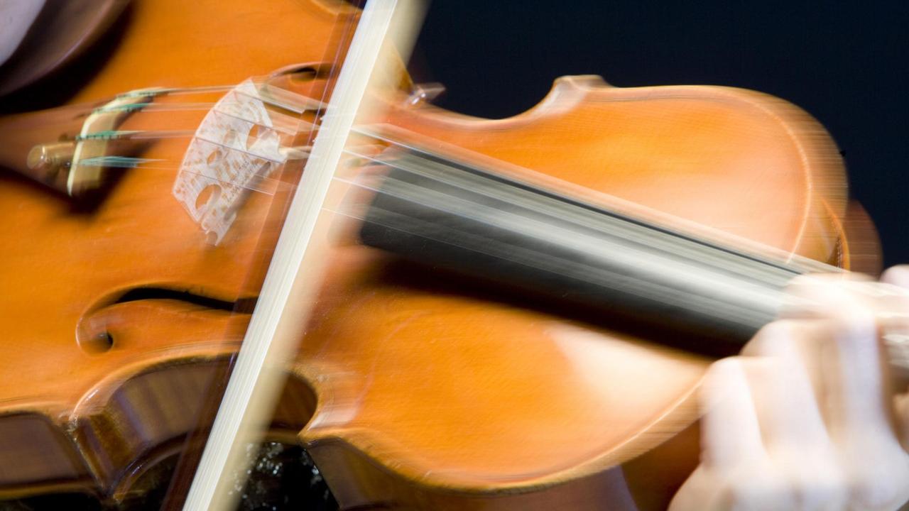 Ein Bogen spielt auf den Saiten einer Geige so schnell, dass er ganz verschwommen auf dem Foto zu sehen ist.