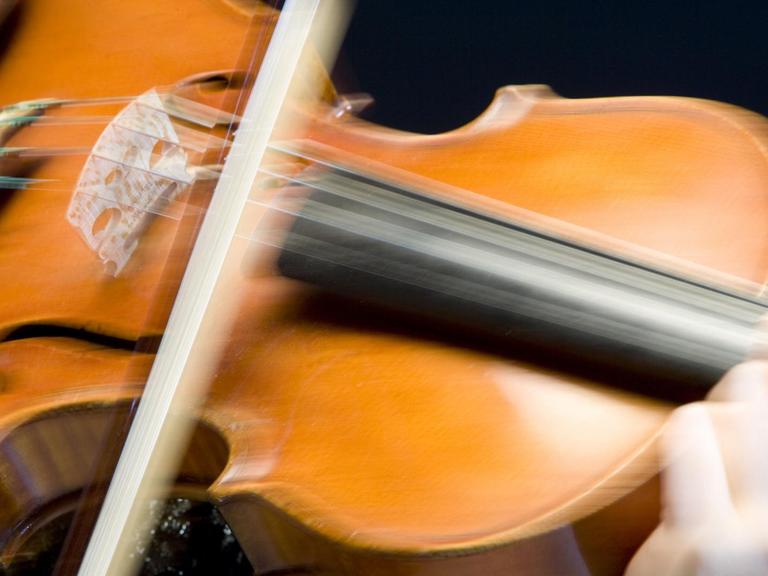 Ein Bogen spielt auf den Saiten einer Geige so schnell, dass er ganz verschwommen auf dem Foto zu sehen ist.