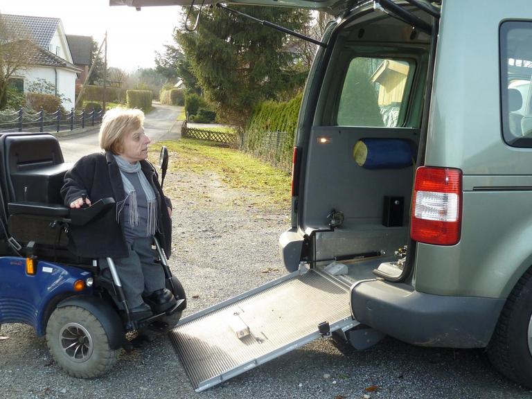 Eine Frau sitzt in einem Rollstuhl und fährt auf einer kleinen Rampe in den hinteren Bereich eines größeren Autos.