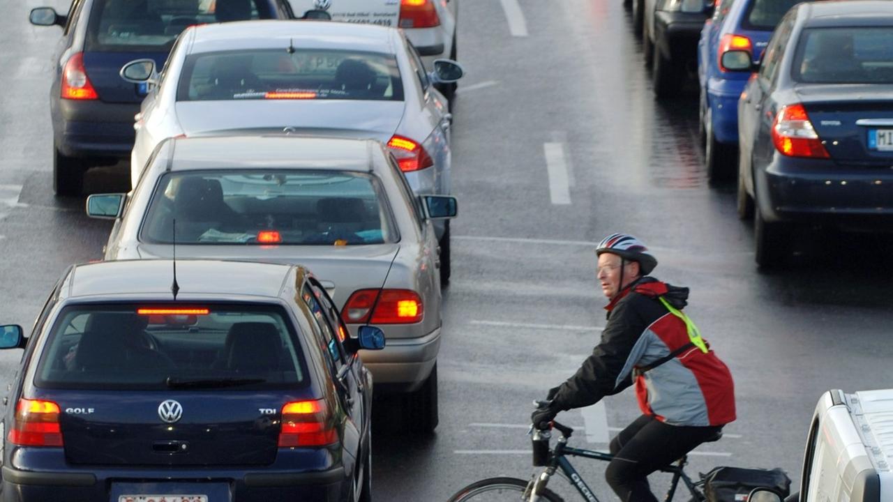 Ein Fahrradfahrer fährt zwischen Autos vorbei, die sich an einer Einfallstraße von Frankfurt am Main im Berufsverkehr stauen. Ein Fahrradfahrer fährt zwischen Autos vorbei, die sich an einer Einfallstraße von Frankfurt am Main im Berufsverkehr stauen.