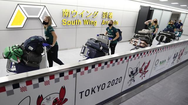 Die Sportlerinnen laufen mit großen Taschen auf Kofferwagen aus dem Flughafen.