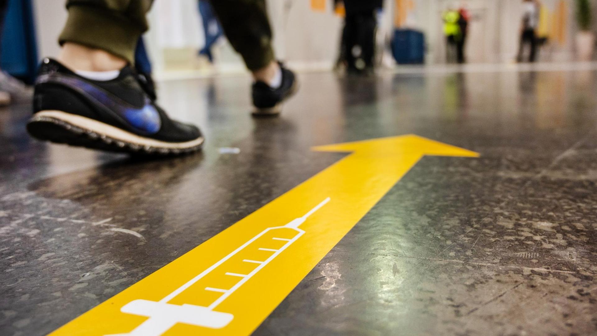 Ein gelber Pfeil auf dem Boden eines Impfzentrums weist Menschen in die richtige Richtung.