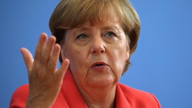 Bundeskanzlerin Angela Merkel in einem rötlichen Jacket gestikuliert mit der rechten Hand.
