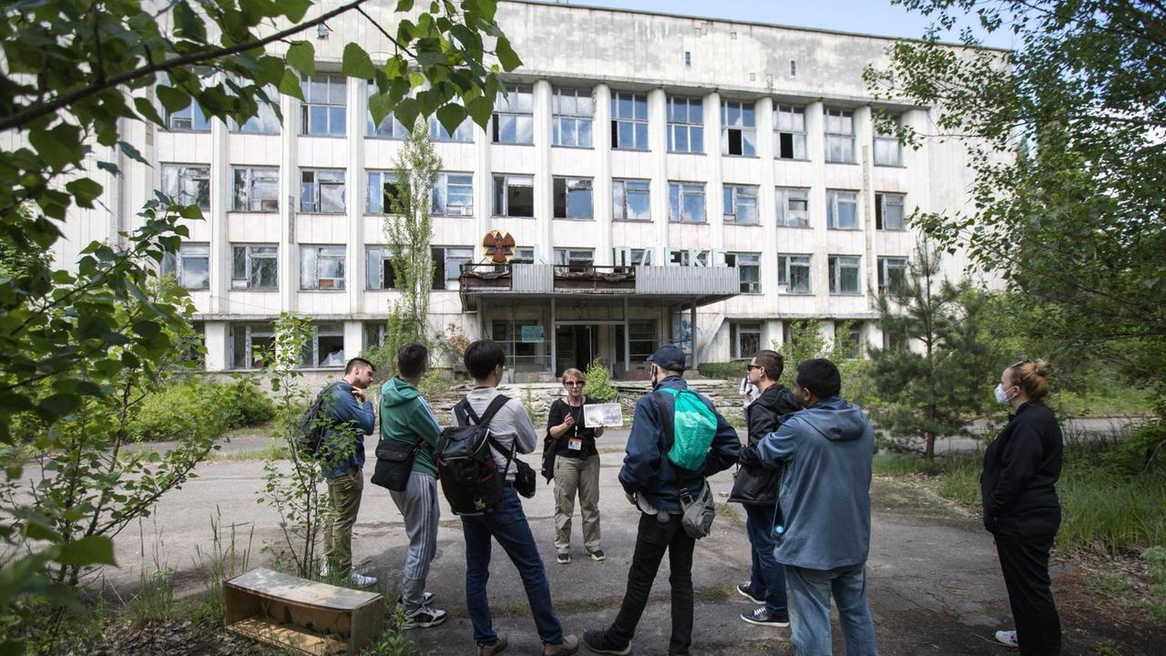 Eine Touristengruppe in der Geisterstadt Pripyat. Im Hintergrund ein verfallenes Haus.
