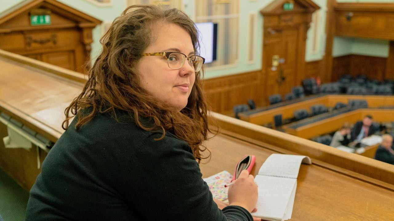 Die Reporterin Caitlin Webb in einem Ratssaal. Die Reporterin Caitlin Webb in einem Ratssaal.