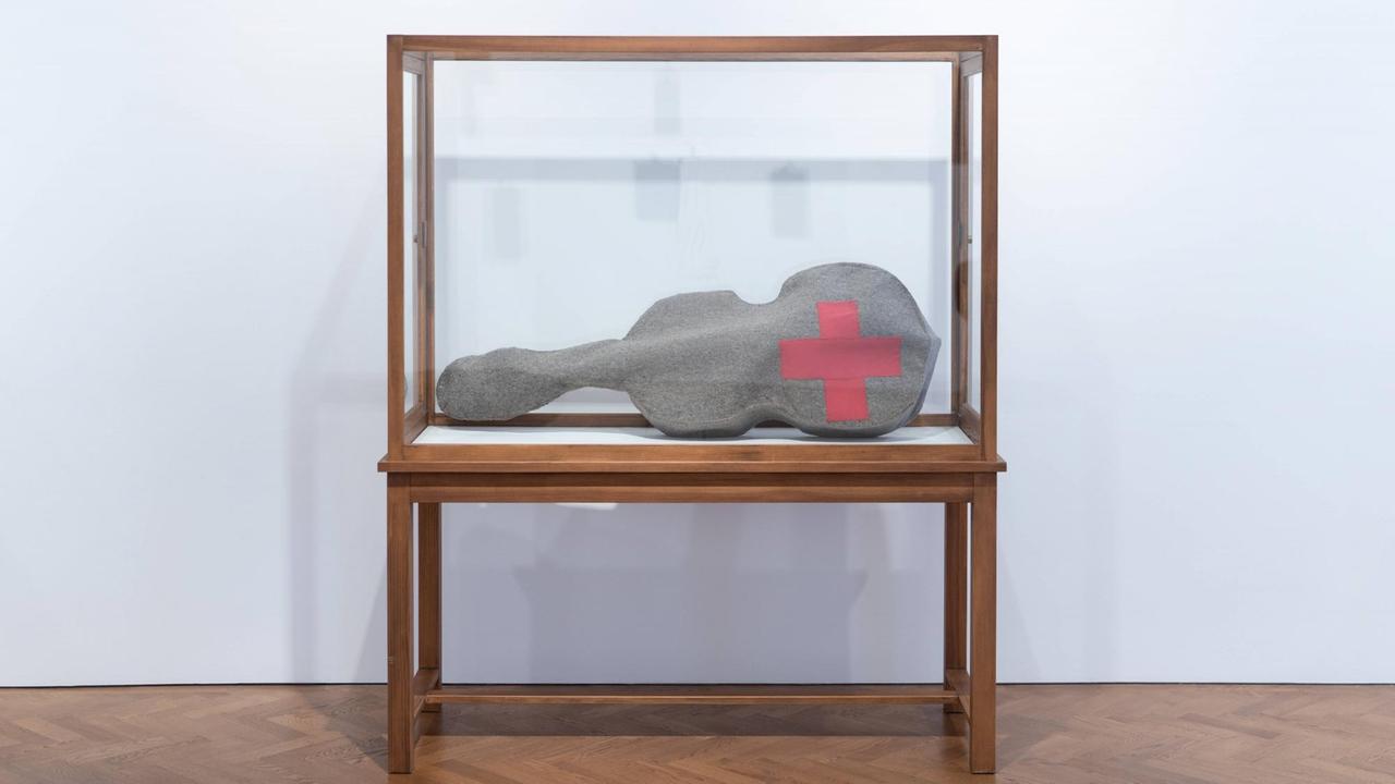 Beuys Arbeit 'Infiltration - Homogen für Cello' besteht aus einer gefilzten Cello-Tasche mit einem roten Kreuz. Hier zu sehen in einer Glasvitrine  während der Ausstellung "The Stag Monuments" in der Galerie Thaddaeus Ropac in London, kuratiert von Norman Rosenthal.