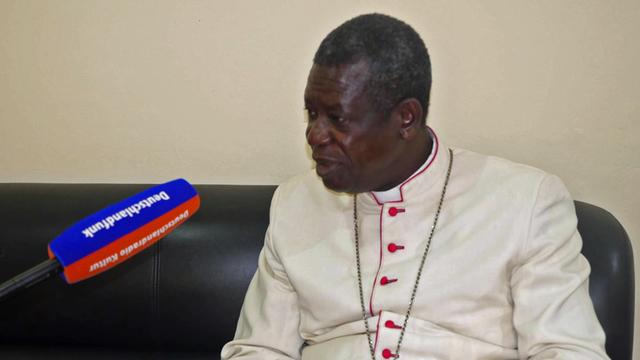 Der Erzbischof von Douala Samuel Kleda sitzt in weißer Soutane auf einer dunkeln Couch beim Interview.