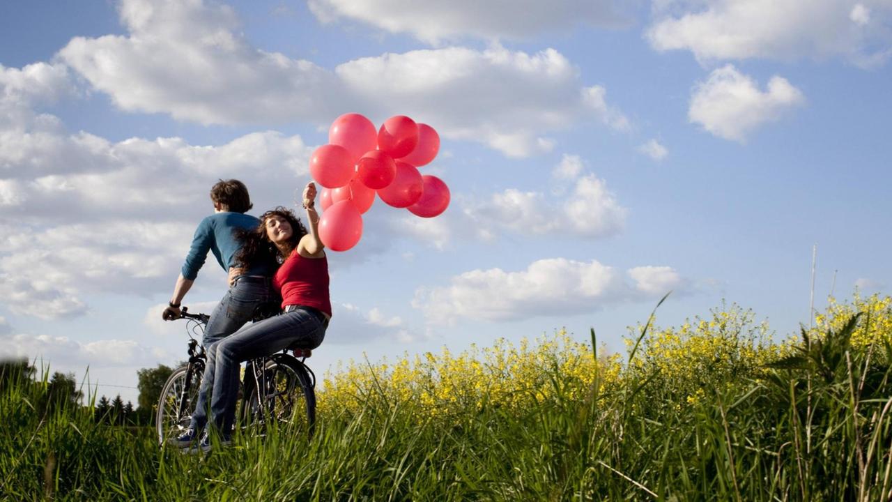 Junges Paar auf einem Fahrrad mit Luftballons Junges Paar auf einem Fahrrad mit Luftballons
