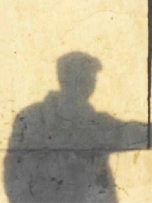 An der Wand sieht man den Schatten eines Mannes, der mit der Hand eine Pistole formt.