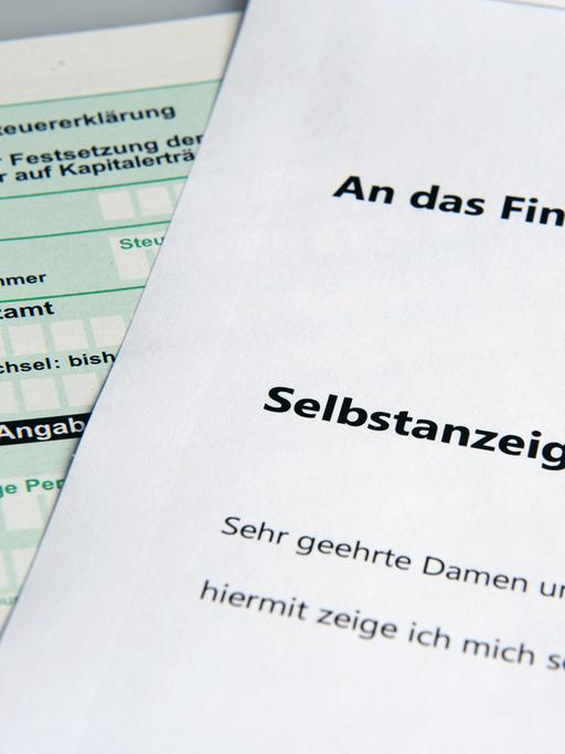 Im Bild ist links ein Steuererklärungsformular und darüber liegend rechts ein weißes Blatt mit dem Titel "Selbstanzeige" zu sehen.