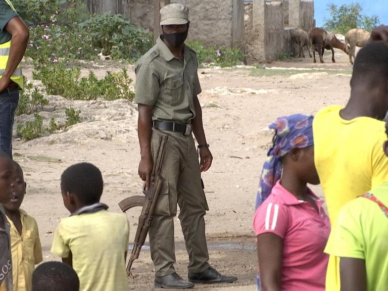 Auf einer Straße steht ein bewaffneter Soldat. Um ihn herum stehen Kinder und Jugendliche.