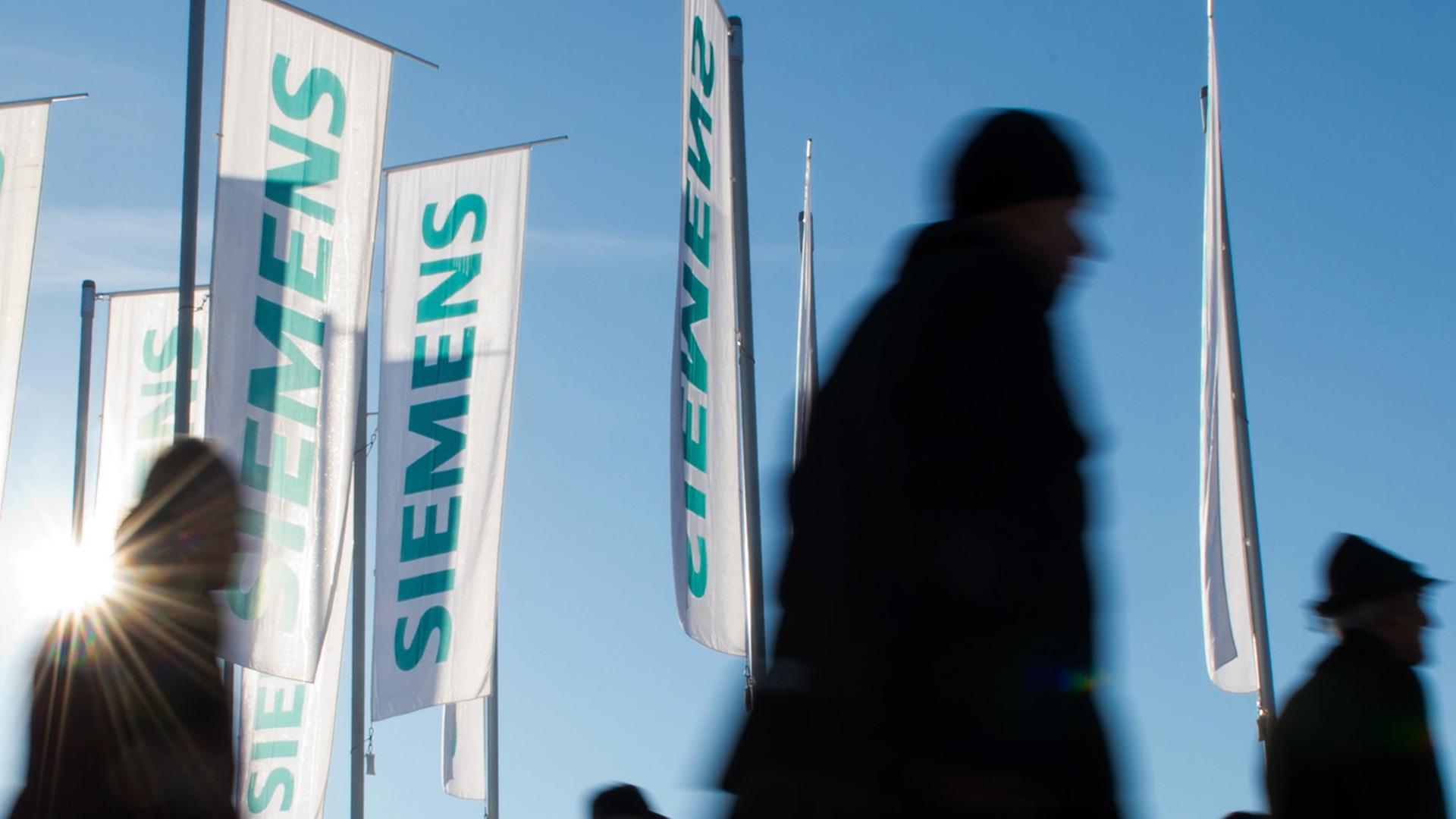 Siemens-Flaggen im Wind, davor laufen Menschen Siemens-Flaggen im Wind, davor laufen Menschen