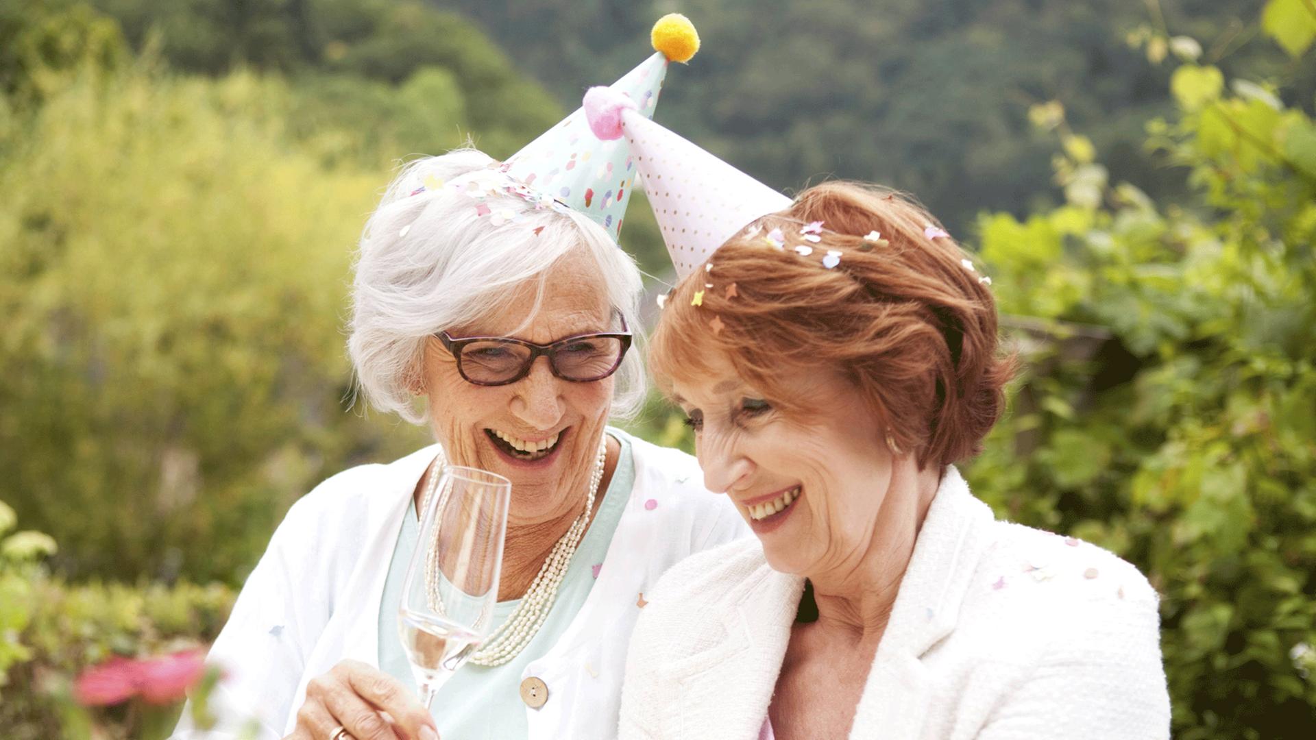 Zwei ältere Frauen trinken auf einer Gartenparty Sekt.