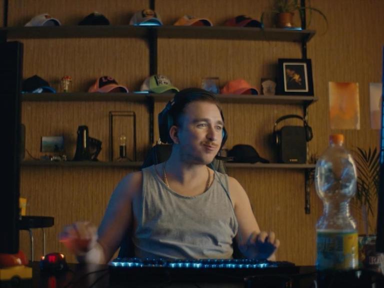 Ein Screenshot vom Corona-Video der Bundesregierung unter dem Titel #besonderehelden - Zusammen gegen Corona - zeigt einen jungen Mann der zwischen zwei Computer-Monitoren an einem Schreibtisch im Unterhemd sitzt und mutmaßlich ein Computerspiel zockt.