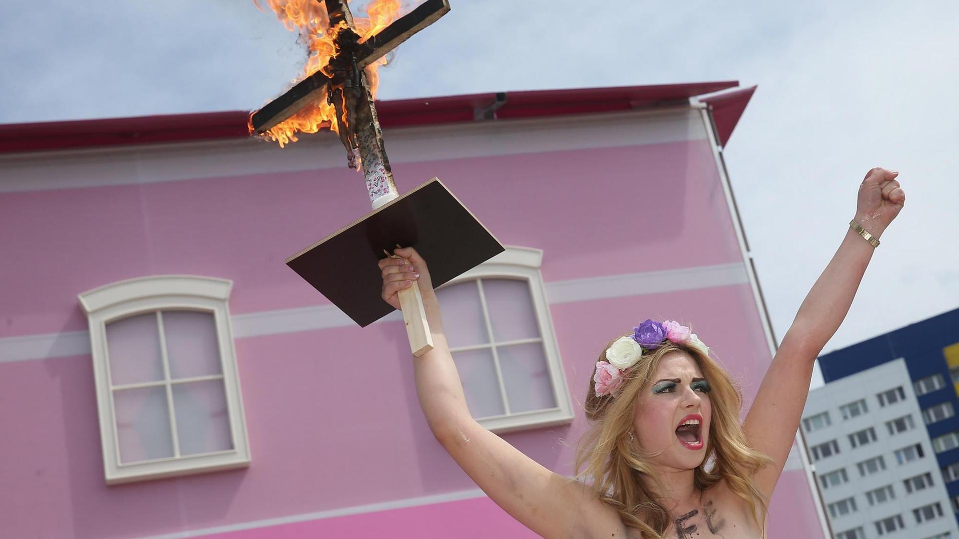 Eine Femen-Demonstrantin mit Blumen im Haar und nackten Brüsten protestiert vor dem Barbie House der Firma Mattel in Berlin, sie hält mit der rechten Hand ein brennendes Kreuz in die Höhe, an das eine Barbie-Puppe gebunden ist, und hat auf ihren Oberkörper die Worte geschrieben: "A Life In Plastic Is Not Fantastic" (Ein Plastik-Leben ist nicht fantastisch). Eine Femen-Demonstrantin mit Blumen im Haar und nackten Brüsten protestiert vor dem Barbie House der Firma Mattel in Berlin, sie hält mit der rechten Hand ein brennendes Kreuz in die Höhe, an das eine Barbie-Puppe gebunden ist, und hat auf ihren Oberkörper die Worte geschrieben: "A Life In Plastic Is Not Fantastic" (Ein Plastik-Leben ist nicht fantastisch).