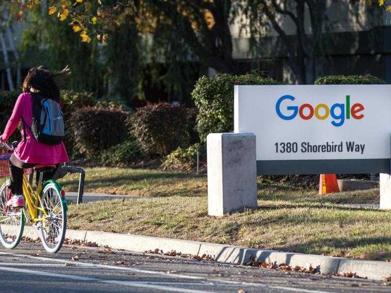 Sie sehen eine Radfahrerin und den Schriftzug Google auf einem Straßenschild.