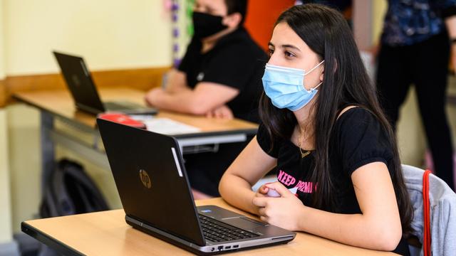 Schülerinnen und Schüler sitzen mit Maske und Laptop im Schulunterricht.