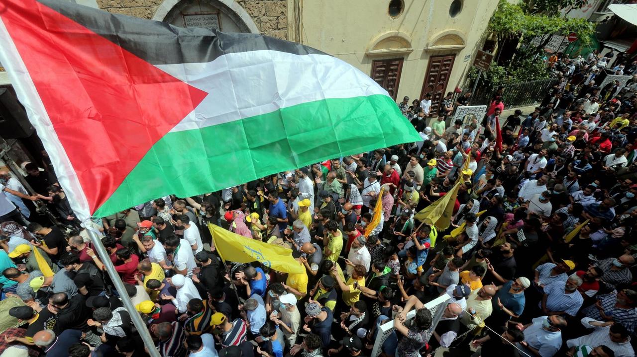 Blick von oben auf eine Demonstration. Am Beginn des Demonstrationszug weht eine Flagge aus Palästina. 