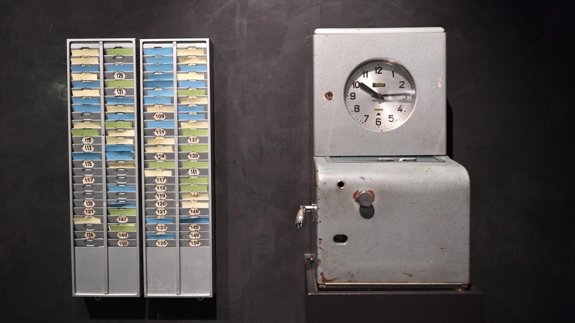 Neben einer Uhr ist ein Kasten an der Wand angebracht, in dem verschiedene Stechkarten stecken. Neben einer Uhr ist ein Kasten an der Wand angebracht, in dem verschiedene Stechkarten stecken.