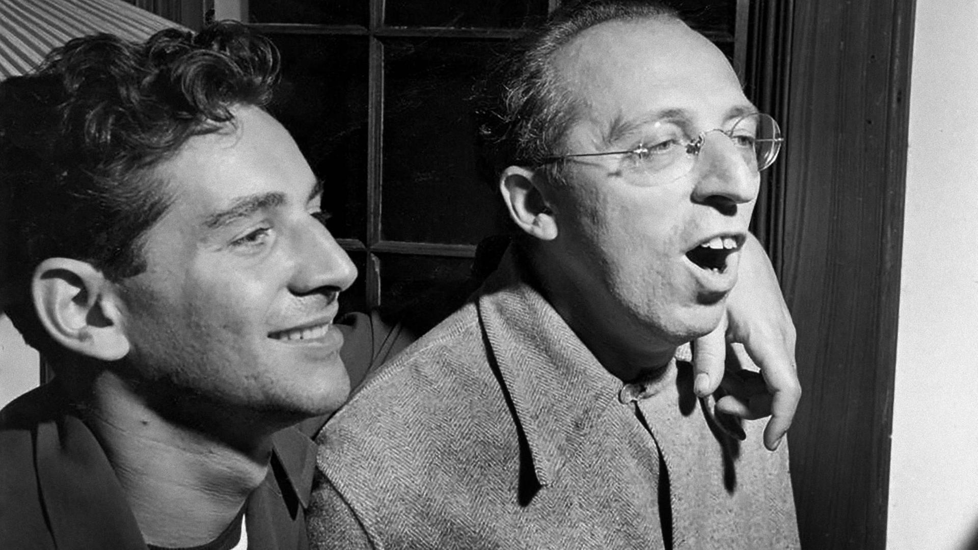 Schwarz-weiß Foto von 1945 mit den Komponisten und Dirigenten Leonard Bernstein und Aaron Copland. Sopland trägt eine runde, randlose Brille und singt offensichtlich Schwarz-weiß Foto von 1945 mit den Komponisten und Dirigenten Leonard Bernstein und Aaron Copland. Sopland trägt eine runde, randlose Brille und singt offensichtlich
