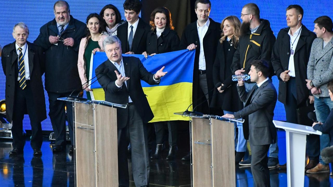 Petro Poroschenko (l.) und Wolodymyr Selenskyj stehen hinter Redepulten auf einer Bühne. Sie liefern sich gestikulierend eine Wahlkampf-Debatte. Im Hintergund sind Mitarbeiter und Sicherheitskräfte zu sehen. Petro Poroschenko (l.) und Wolodymyr Selenskyj stehen hinter Redepulten auf einer Bühne. Sie liefern sich gestikulierend eine Wahlkampf-Debatte. Im Hintergund sind Mitarbeiter und Sicherheitskräfte zu sehen.