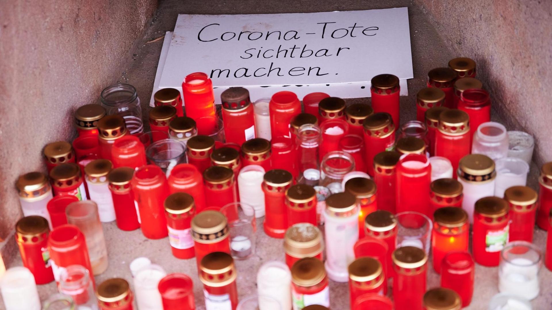 "Corona-Tote sichtbar machen" steht auf einem Karton, der von Totenlämpchen umringt ist. Eine private Initiative erinnert so an die aktuelle Zahl der Corona-Toten. "Corona-Tote sichtbar machen" steht auf einem Karton, der von Totenlämpchen umringt ist. Eine private Initiative erinnert so an die aktuelle Zahl der Corona-Toten.