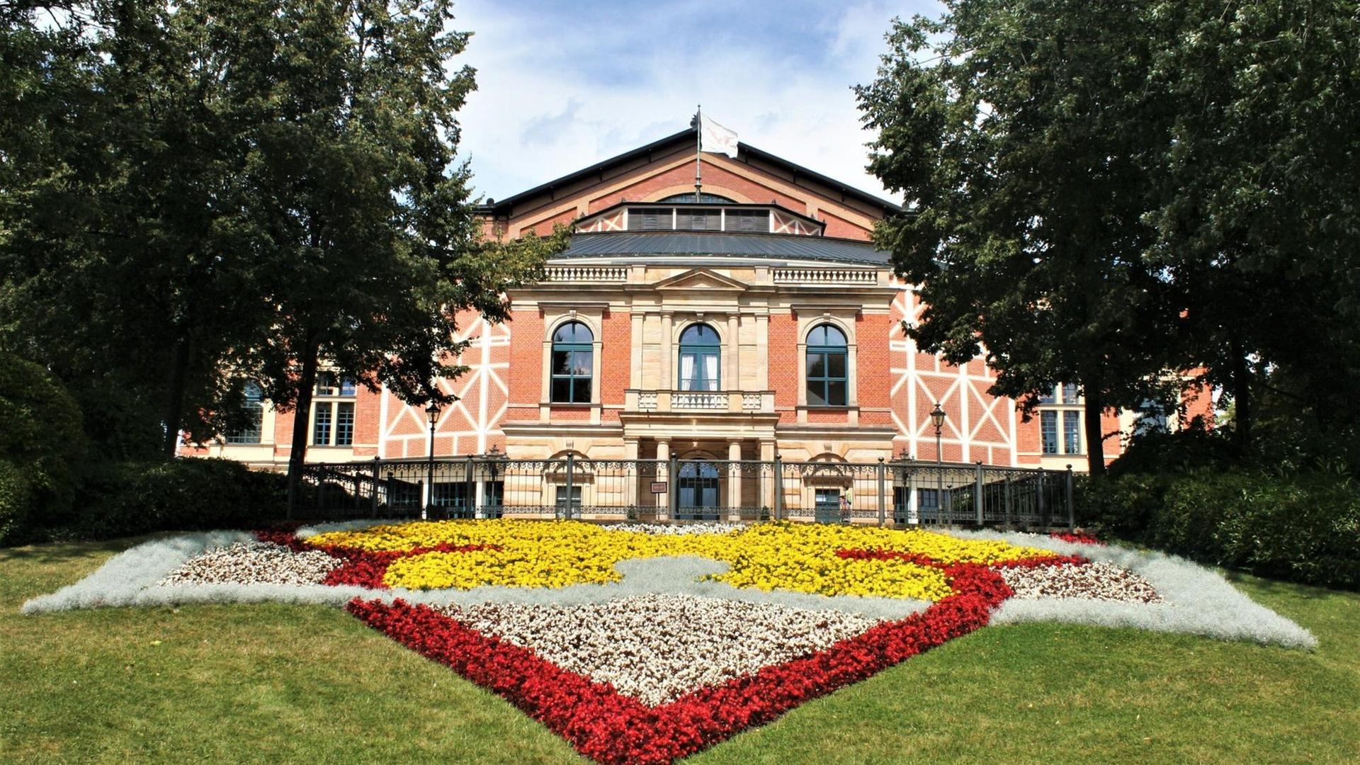 Außenaufnahme des Bayreuther Festspielhauses mit einem großen bunten Blumenbeet im Vordergrund