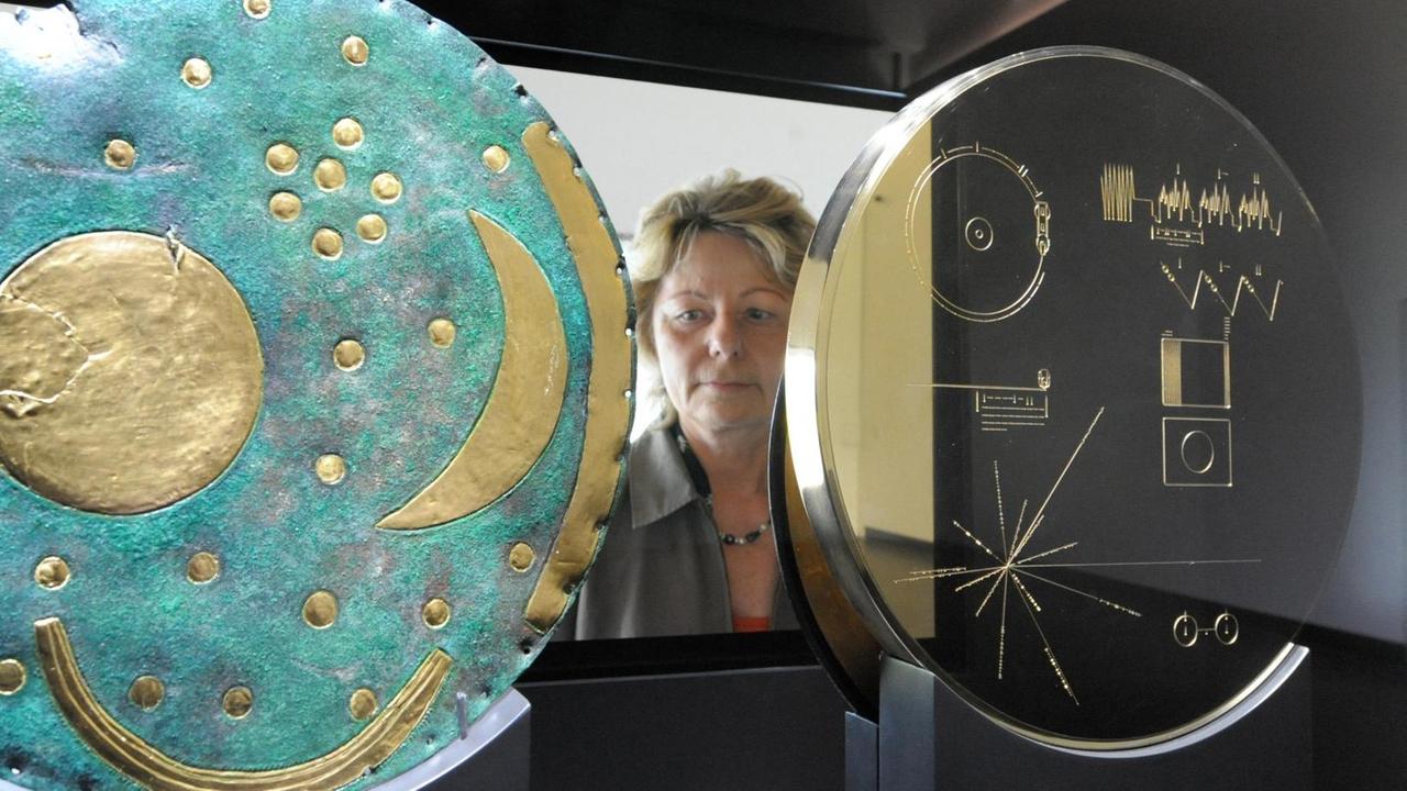 Die Rückseite der Himmelsscheibe von Nebra (l) und die Scheibe "Voyager Golden Record" betrachtet eine Besucherin in der Ausstellung "Codiert für die Ewigkeit" im Besucherzentrum Arche Nebra am Mittwoch (29.04.2009) in Wangen (Burgenlandkreis). Die Masterkopie der Himmelsscheibe steht erstmals neben der Kopie der "Voyager Golden Record", die im Original 1977 als Datenplatte mit US-Raumsonden ins All geschickt worden ist. 