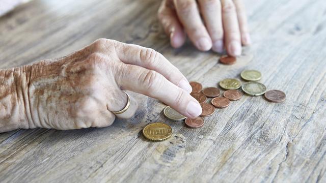 Die Hand einer älteren Frau schiebt ein paar Münzen auf einer Tischplatte herum