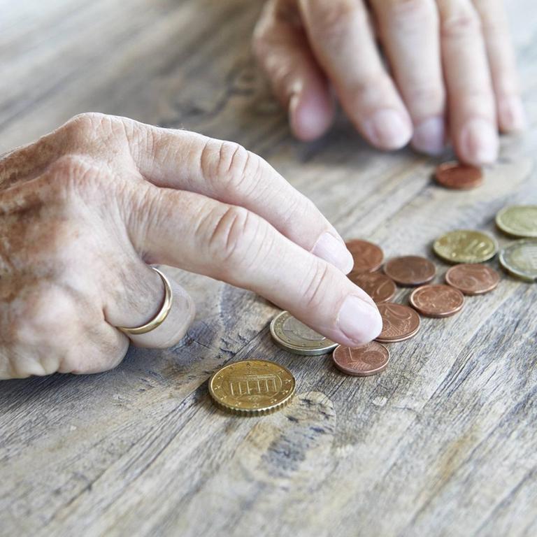 Die Hand einer älteren Frau schiebt ein paar Münzen auf einer Tischplatte herum