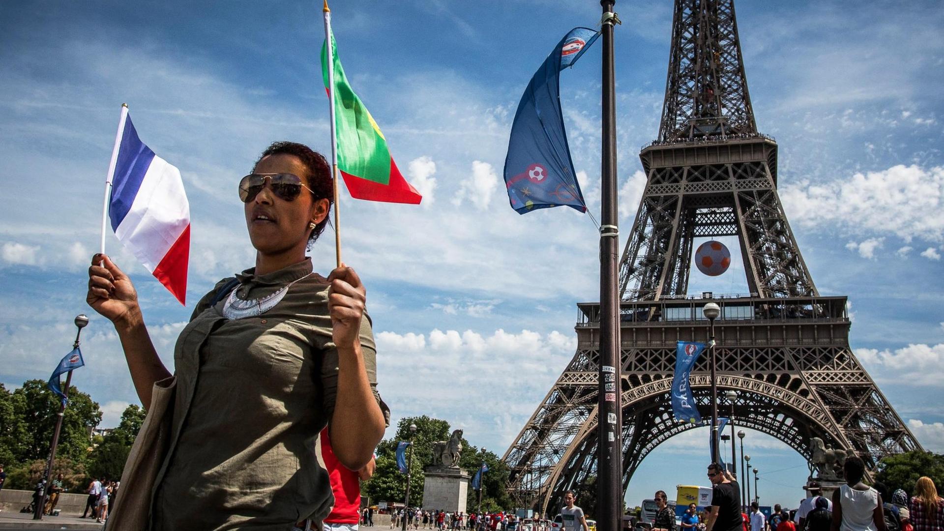 Eine Frau mit einer französischen und einer portugiesischen Flagge in der Hand läuft vor dem Eiffelturm entlang.