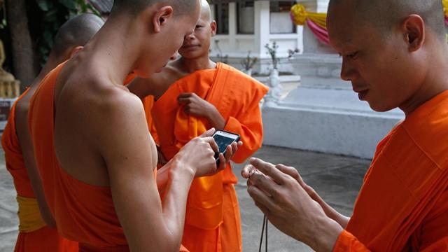 Buddhistische Mönche in Laos schauen auf ihre Smartphones und Kameras.