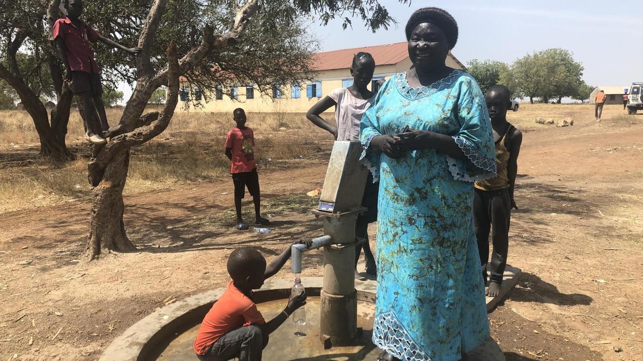 Lehrerin Grace mit Schülern an der Wasserpumpe auf dem Gelände einer Schule in Juba, Südsudan