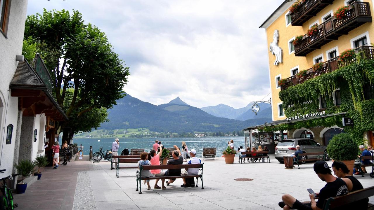 Der Schiffsanlegeplatz in St. Wolfgang am Wolfgangsee. Mehrere Menschen sitzen auf Bänken oder gehen durch die Fußgängerzone am Seeufer. Der Schiffsanlegeplatz in St. Wolfgang am Wolfgangsee. Mehrere Menschen sitzen auf Bänken oder gehen durch die Fußgängerzone am Seeufer.