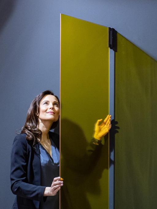 Ein Frau steht auf der Messe in einem arrangierten Badezimmer mit grauer Wand und einer gelben Glasduschtür.