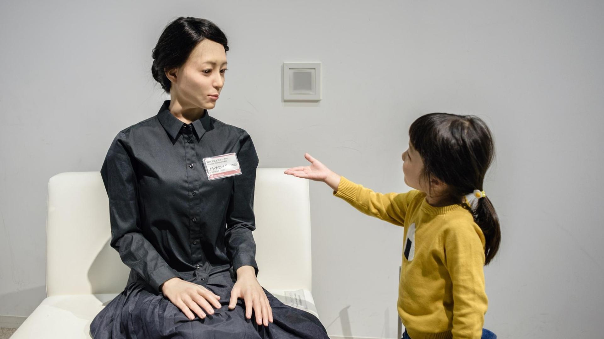 Ein junges Mädchen streckt einem weiblich aussehenden Roboter die Hand entgegen. Ein junges Mädchen streckt einem weiblich aussehenden Roboter die Hand entgegen.