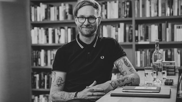 Schwarz-Weiß-Fotografie des Psychologen Frank Berzbach vor einem Bücherregal. Schwarz-Weiß-Fotografie des Psychologen Frank Berzbach vor einem Bücherregal.